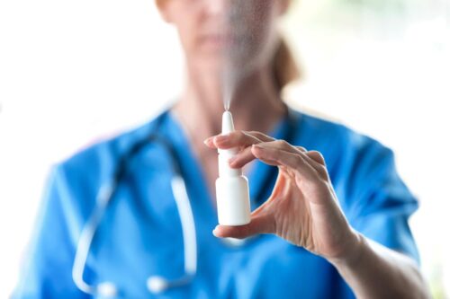 Nasal Spray Company Pushes CDC, FDA to Accept Its Claims to Help Treat COVID Close-up of female doctor with a spray or nasal drops for the treatment of a runny nose over white background.