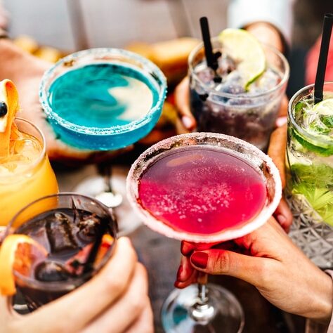 People hands toasting multicolored fancy drinks - Young friends having fun together drinking cocktails at happy hour - Social gathering party time concept on warm vivid filter