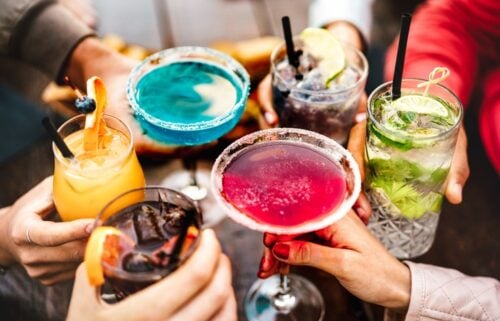 Risky Drinking Common in Cancer Survivors People hands toasting multicolored fancy drinks - Young friends having fun together drinking cocktails at happy hour - Social gathering party time concept on warm vivid filter