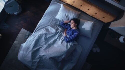 Sleeping Beats Sitting? What a New Study Means for Patients Top View of Beautiful Young Woman Sleeping Cozily on a Bed in Her Bedroom at Night. Comfortable Apartment with Sweet Girl Resting when Moonlight Shining Through Apartment Window. Top Down